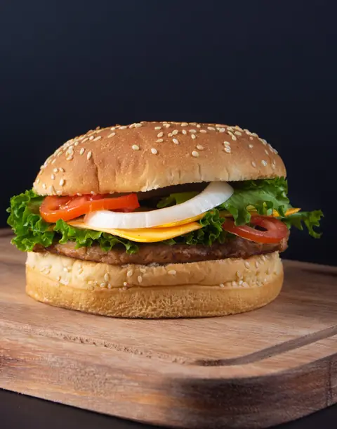 Hamburguesa con queso amarillo, cebolla, jitomate y lechuga en pan con ajonjolí