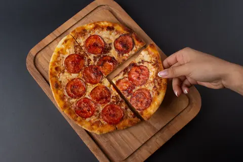Pizza de pepperoni en cuartos sobre tabla de madera