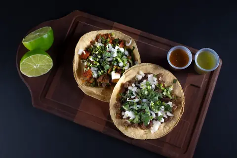 Dos tacos con cebolla y cilantro, limones y salsas roja y verde