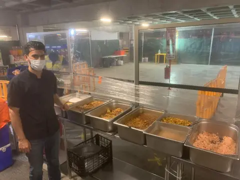 Integrante del equipo junto a charolas de comida caliente en un comedor de obra