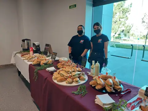 Dos integrantes del equipo junto a una mesa montada con bocadillos